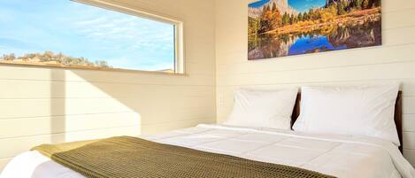 A bedroom with a large bed, a window, and a painting of a mountain landscape.