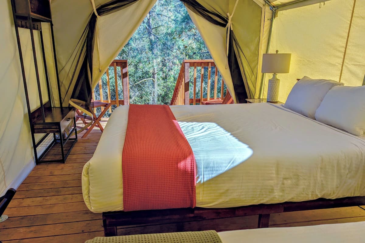 Ein Zelt mit Bett, einer Holzterrasse und Blick auf Bäume.
