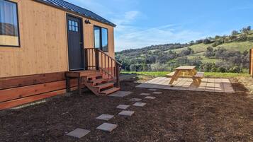 A wooden cabin with a porch, a picnic table, and a view of a hilly landscape.