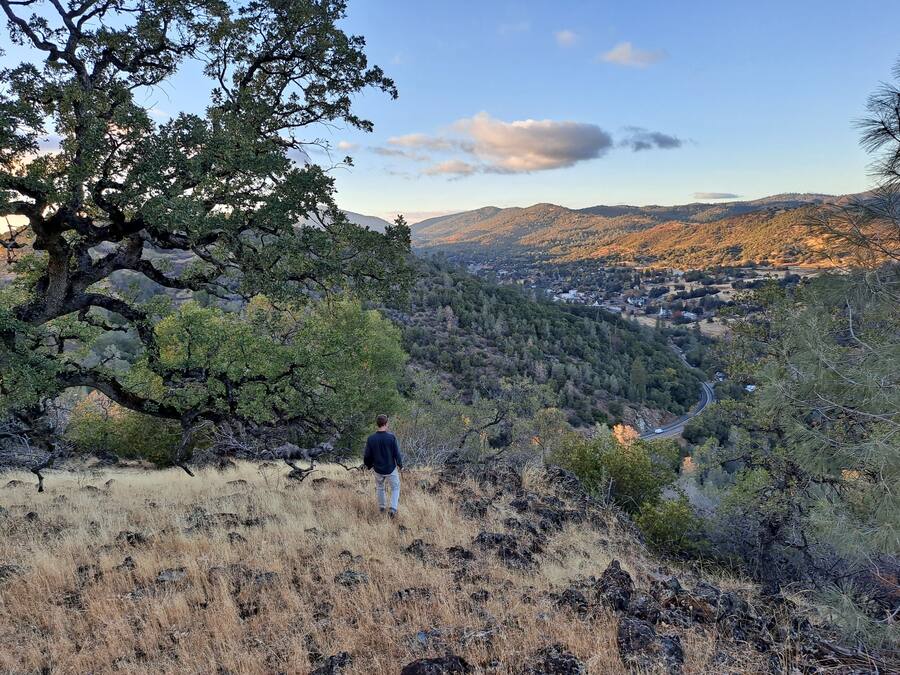 A person walking on a hillside with a view of a valley and distant hills.