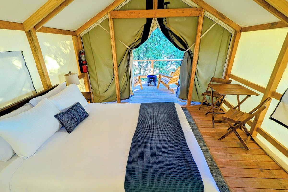 Eine Zelteinrichtung mit Bett, einem kleinen Tisch und Blick ins Freie.