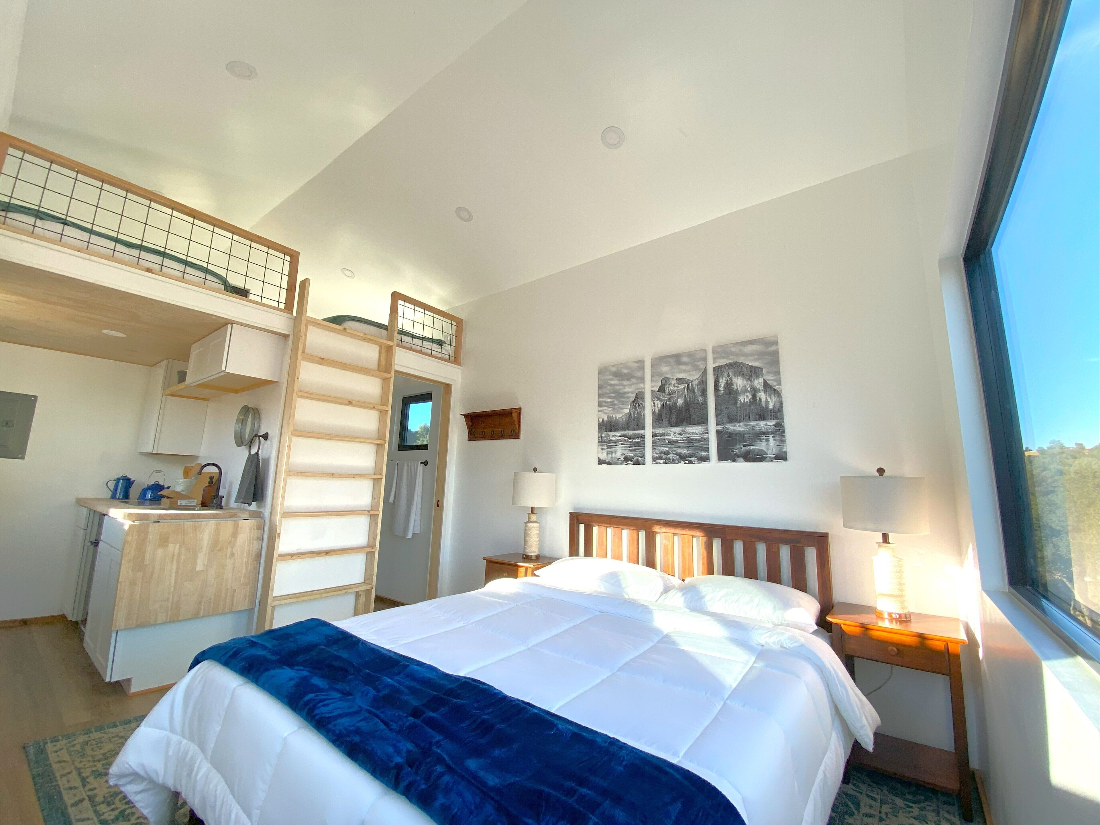 A bedroom with a bed, a desk, a ladder, a window, and a wall-mounted picture.