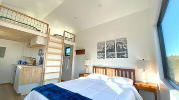 A bedroom with a bed, a desk, a ladder, a window, and a wall-mounted picture.