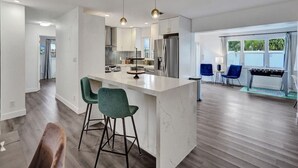 Una cocina moderna con una isla central, taburetes de bar y una zona de comedor con sillas azules.