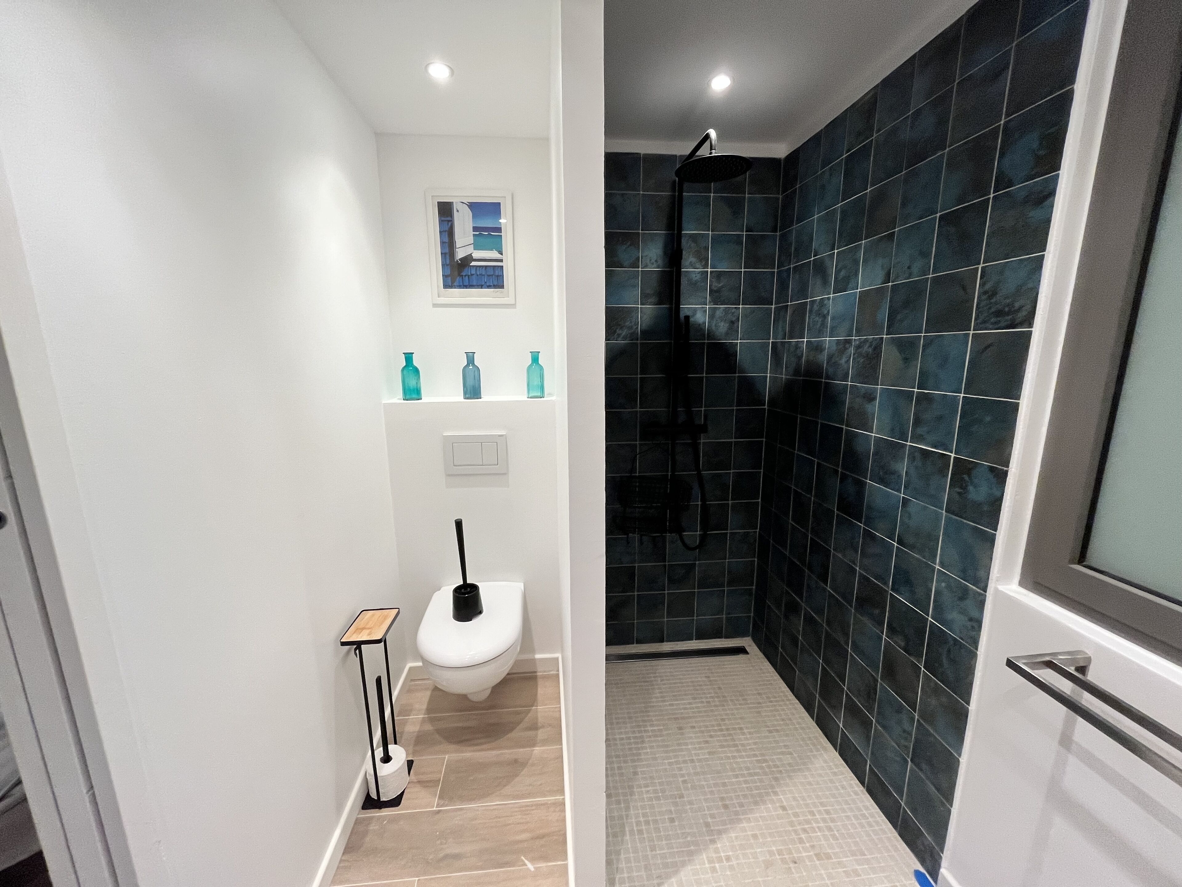 Ein modernes Badezimmer mit Dusche, Toilette und einer kleinen Ablage mit Flaschen.