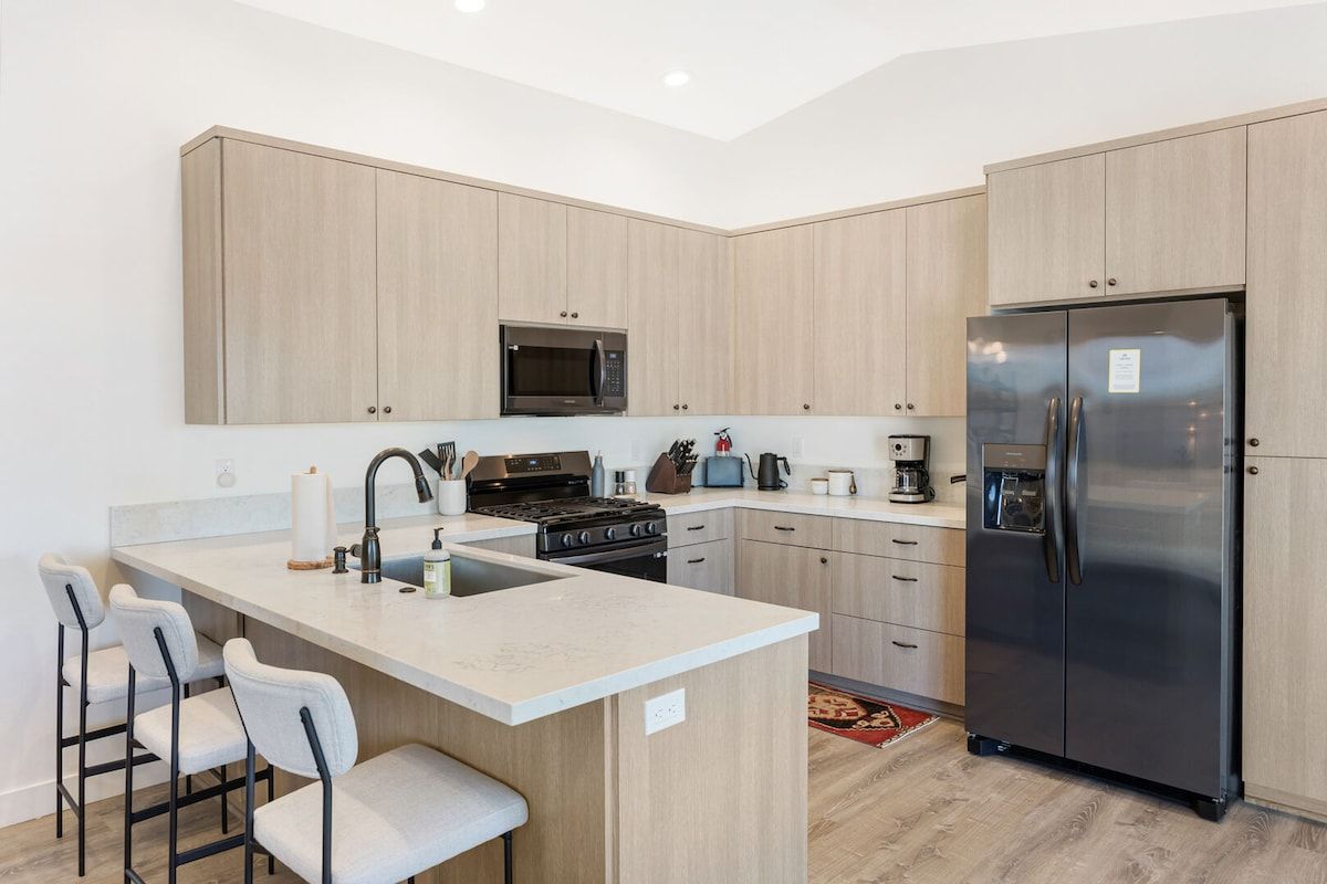 Una cocina moderna con una isla central, taburetes de bar, un refrigerador de acero inoxidable y armarios de madera.