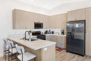 Een moderne keuken met een centraal eiland, barstoelen, een roestvrijstalen koelkast en houten kastjes.