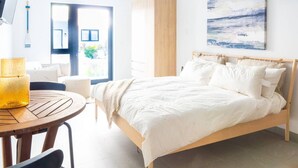 A bedroom with a bed, a round wooden table with a yellow lamp, a wardrobe, and a painting on the wall. - 25% Off Sept 10-12! Walk 2 Beach, Pool  Z-B103 (Grace Bay)