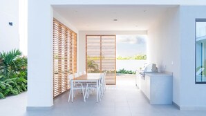 Un espace de restauration extérieur moderne, avec une table et des chaises, un barbecue et une vue sur la verdure.
