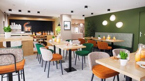 Een modern café met houten tafels en stoelen, een koffieapparaat en een groene wand met ronde verlichting.