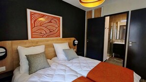 Een hotelkamer met een groot bed, een houten hoofdbord, een aan de muur hangend kunstwerk, een nachtkastje en een deur naar een badkamer.