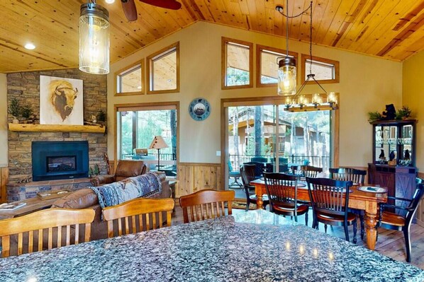 Un salon spacieux doté d’une cheminée, de grandes fenêtres et d’un coin repas avec des meubles en bois.