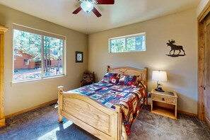 A bedroom with a wooden bed, a nightstand, a ceiling fan, and two windows. - Pristine Torreon Cabin, Sleeps 6 (Show Low)