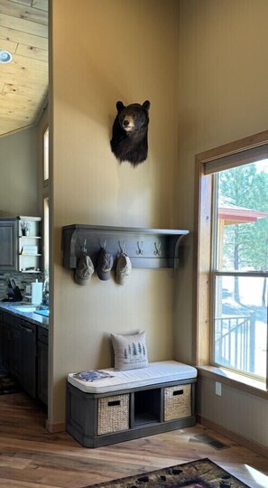 Une pièce décorée d’une tête d’ours fixée au mur, d’un porte-manteau avec des chapeaux, d’un banc muni de paniers de rangement et d’une fenêtre donnant sur des arbres.