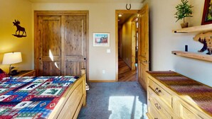 A room with a wooden door, a bed with a colorful quilt, a small table with a lamp, and a shelf with decorative items. - Pristine Torreon Cabin, Sleeps 6 (Show Low)