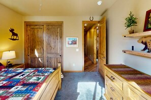 A room with a wooden door, a bed with a colorful quilt, a small table with a lamp, and a shelf with decorative items. - Pristine Torreon Cabin, Sleeps 6 (Show Low)