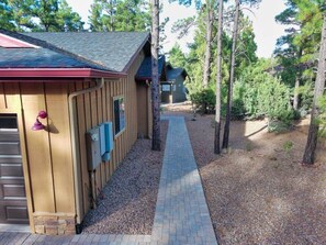 A wooden building with a red roof, a brick pathway leading to it, and a forested area in the background. - Pristine Torreon Cabin, Sleeps 6 (Show Low)