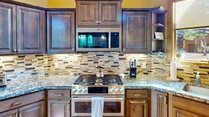 A kitchen with dark wood cabinets, a stainless steel range, a microwave, and a tiled backsplash. - Pristine Torreon Cabin, Sleeps 6 (Show Low)