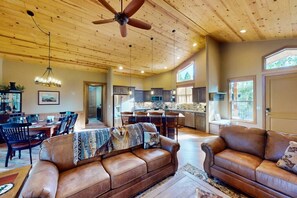 A spacious living room with a large brown leather sofa, a dining area with a wooden table and chairs, and a kitchen with wooden cabinets and a large island. - Pristine Torreon Cabin, Sleeps 6 (Show Low)