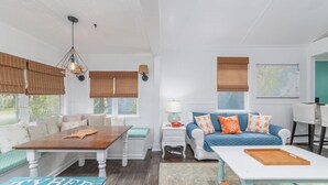 A cozy living room with a wooden table, a blue sofa with orange pillows, and a white armchair. - Darling Beach House with Private Pool! (Tybee Island)