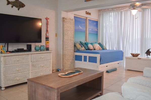 Un dormitorio con cama, televisor, cómoda y ventana con cortinas.