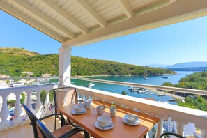 Enjoy a meal on the balcony with a view of the coastal area, featuring a body of water and hilly landscape.