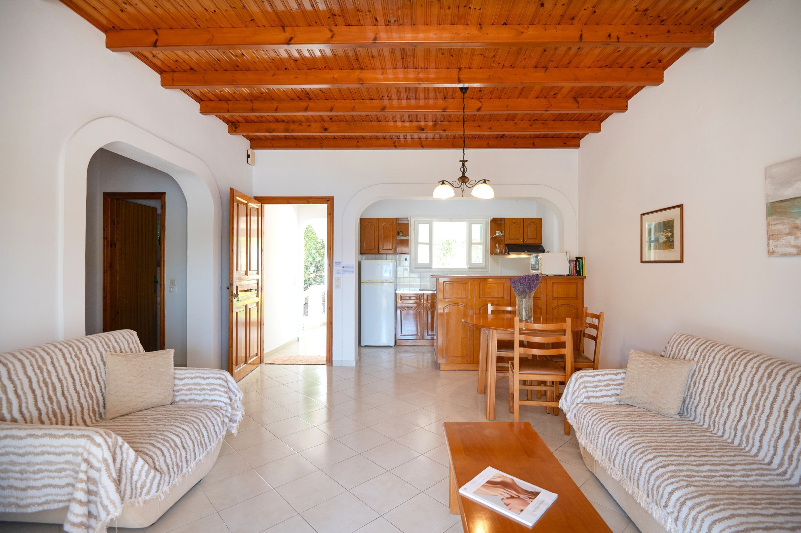 Amplia sala de estar con techo de madera, una cocina al fondo y un comedor con mobiliario de madera.