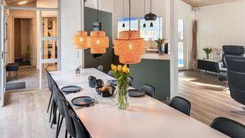 Et moderne spiseområde med et langt bord, sorte stole og orange vævede pendellamper.