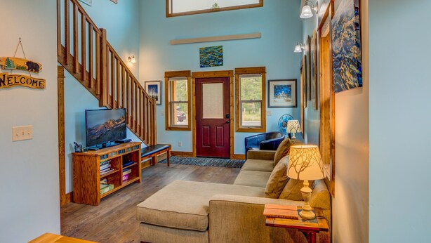 A living room with a wooden staircase, a television, a sofa, and a coffee table. - Barnes on Boundary Unit A (West Yellowstone)