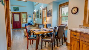 A dining area with a wooden table set for four, surrounded by chairs. There is a red door and a window with a view of the outdoors. - Barnes on Boundary Unit A (West Yellowstone)