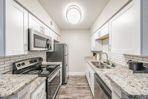 A modern kitchen with white cabinets, a stainless steel refrigerator, a microwave, a stove, and granite countertops.