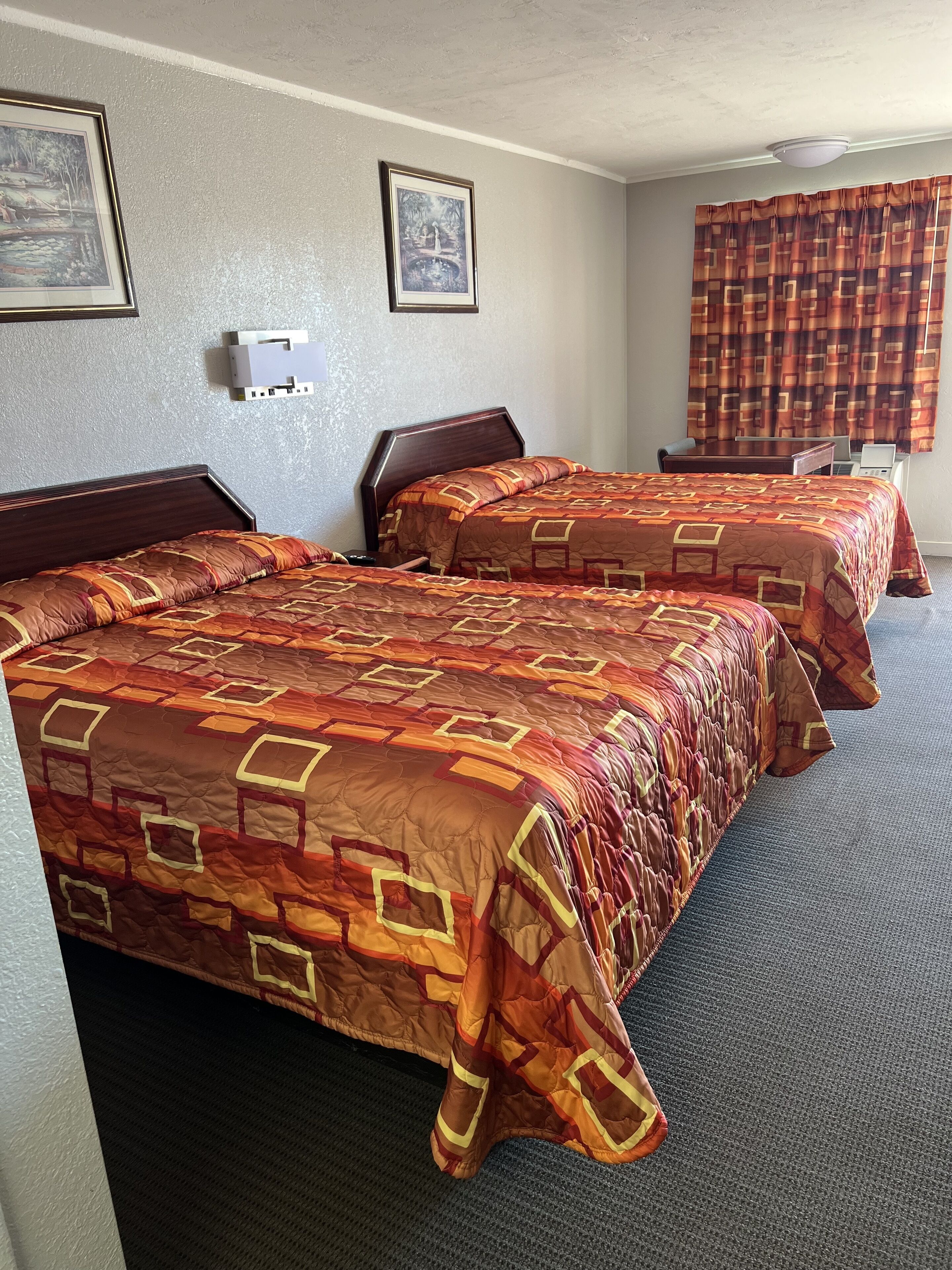 A hotel room with two beds, a desk, a chair, a laptop, and a window with curtains.
