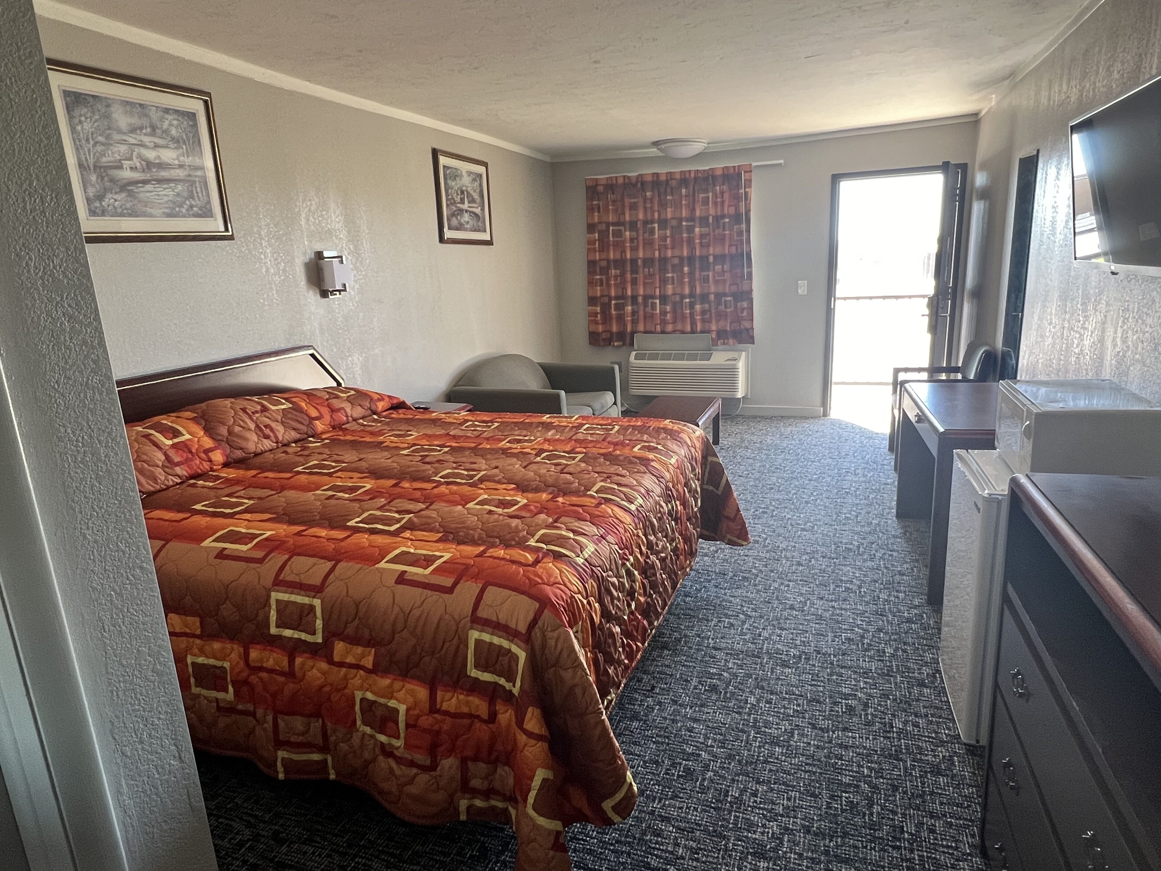 A hotel room with a large bed, a desk, a chair, a dresser, and a television.
