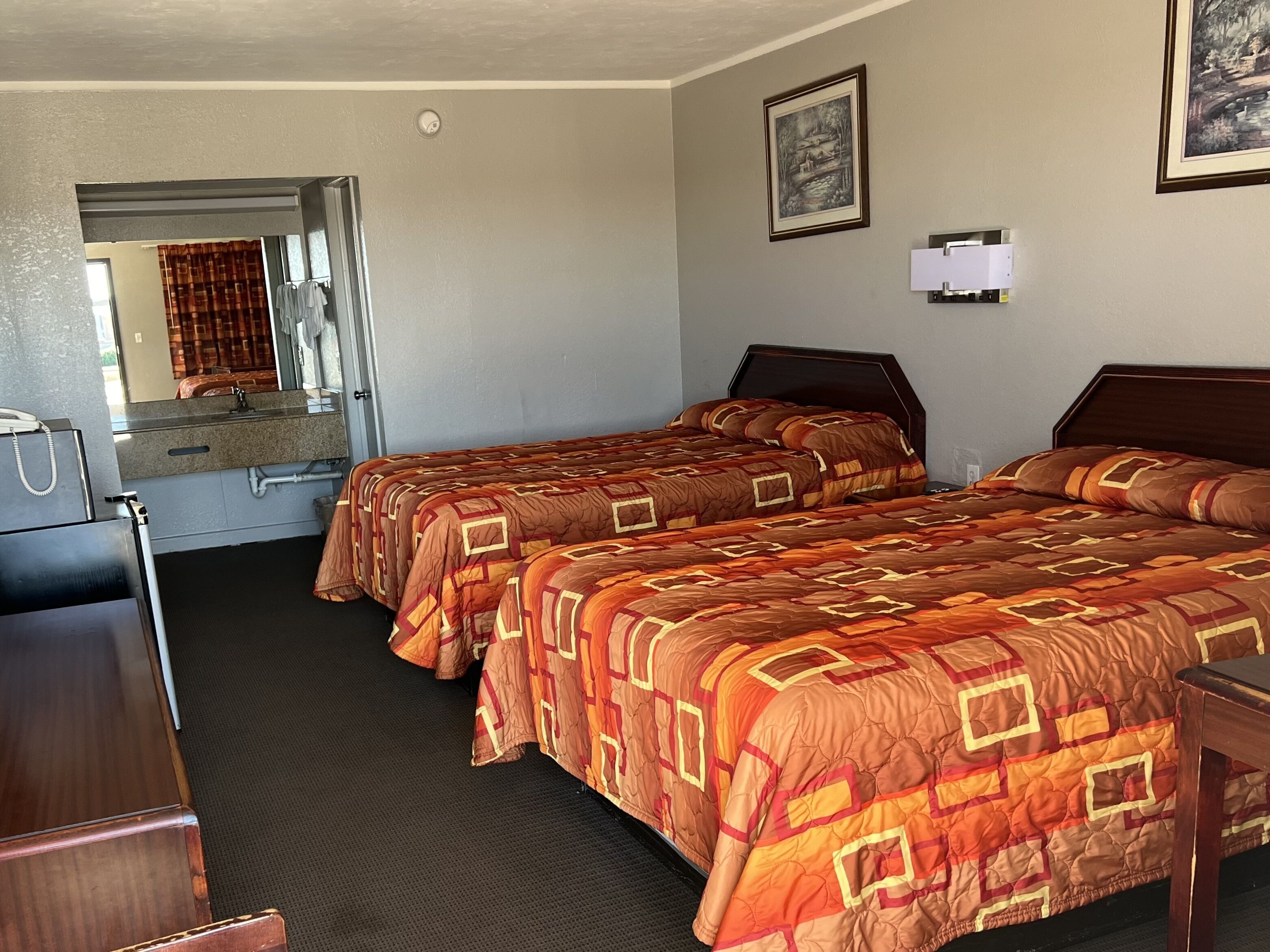 A hotel room with two beds, a desk, a mirror, and a framed picture on the wall.