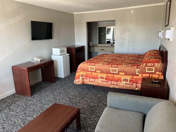 A hotel room with a bed, a desk, a chair, a TV, a microwave, and a small refrigerator.