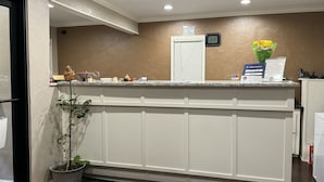 A reception area with a counter, a clock, a sign indicating check-out time, a plant, and a vase with flowers. - Hotel 81 El Reno (El Reno)