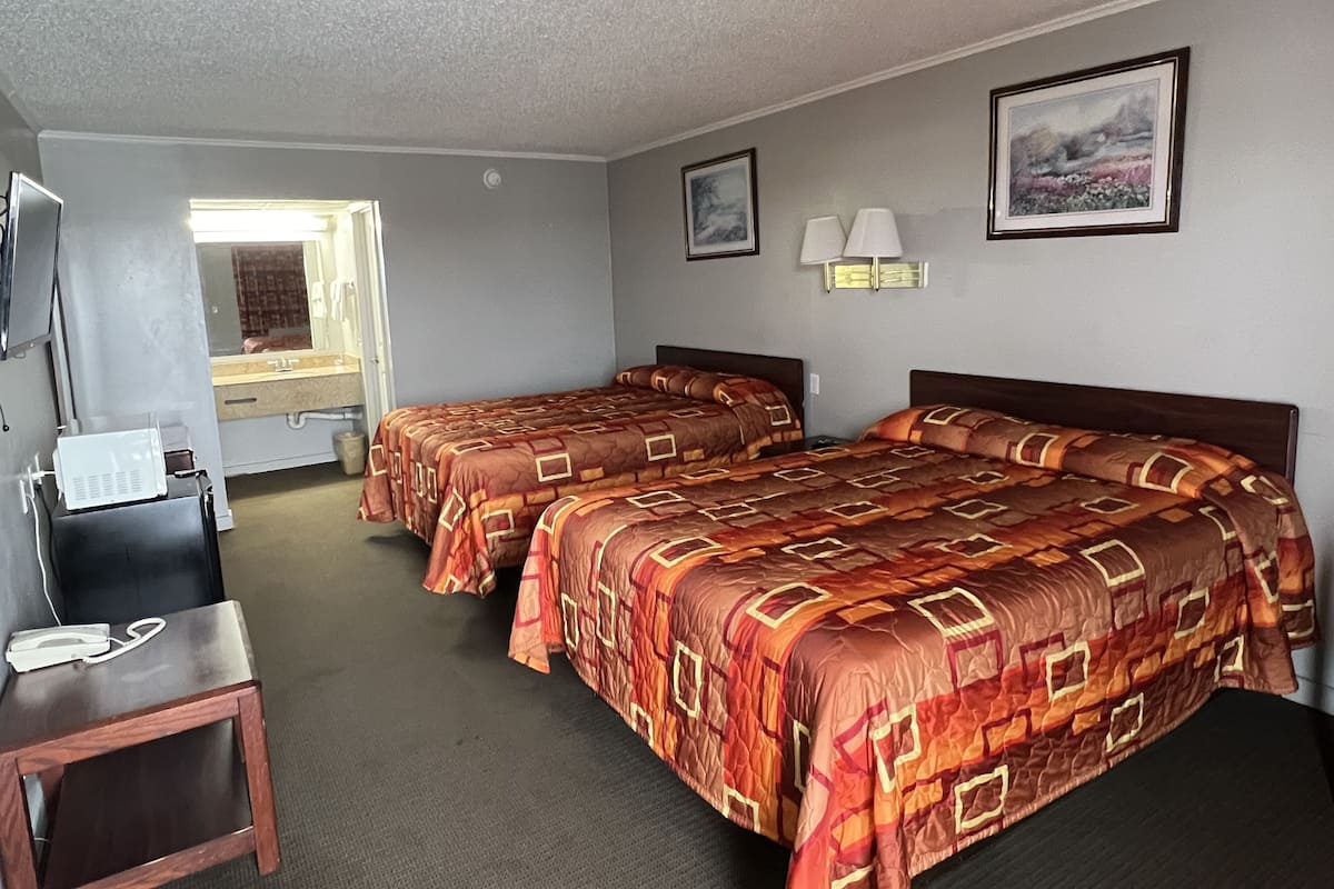 A hotel room with two beds, a desk, a chair, a TV, and a bathroom visible through an open door.
