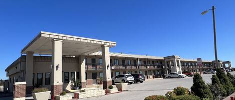 A multi-story hotel with a covered parking area, multiple balconies, and a clear blue sky.