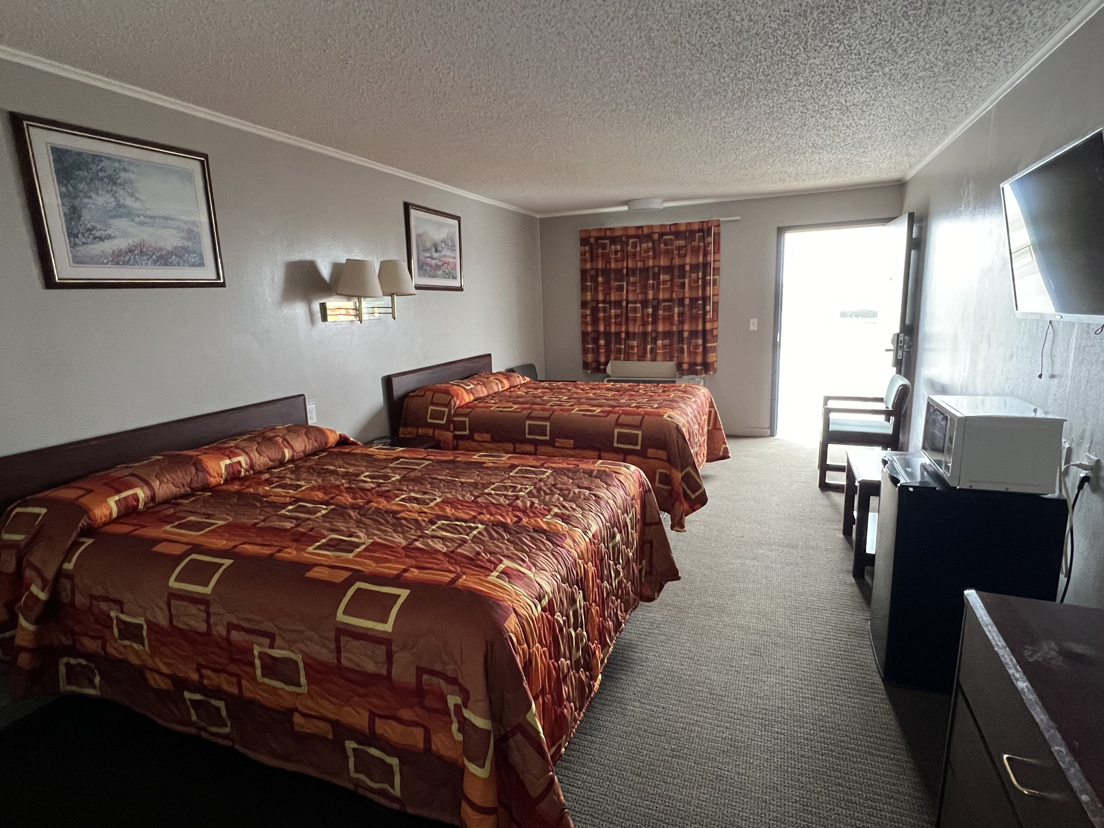 Une chambre d’hôtel avec deux lits, un bureau, une télévision et une fenêtre avec des rideaux.