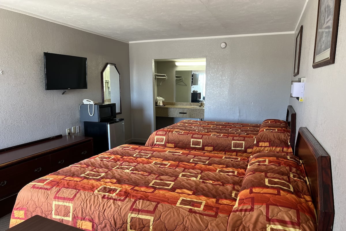 A hotel room with a large bed, a dresser, a television, and a bathroom visible through an open door.