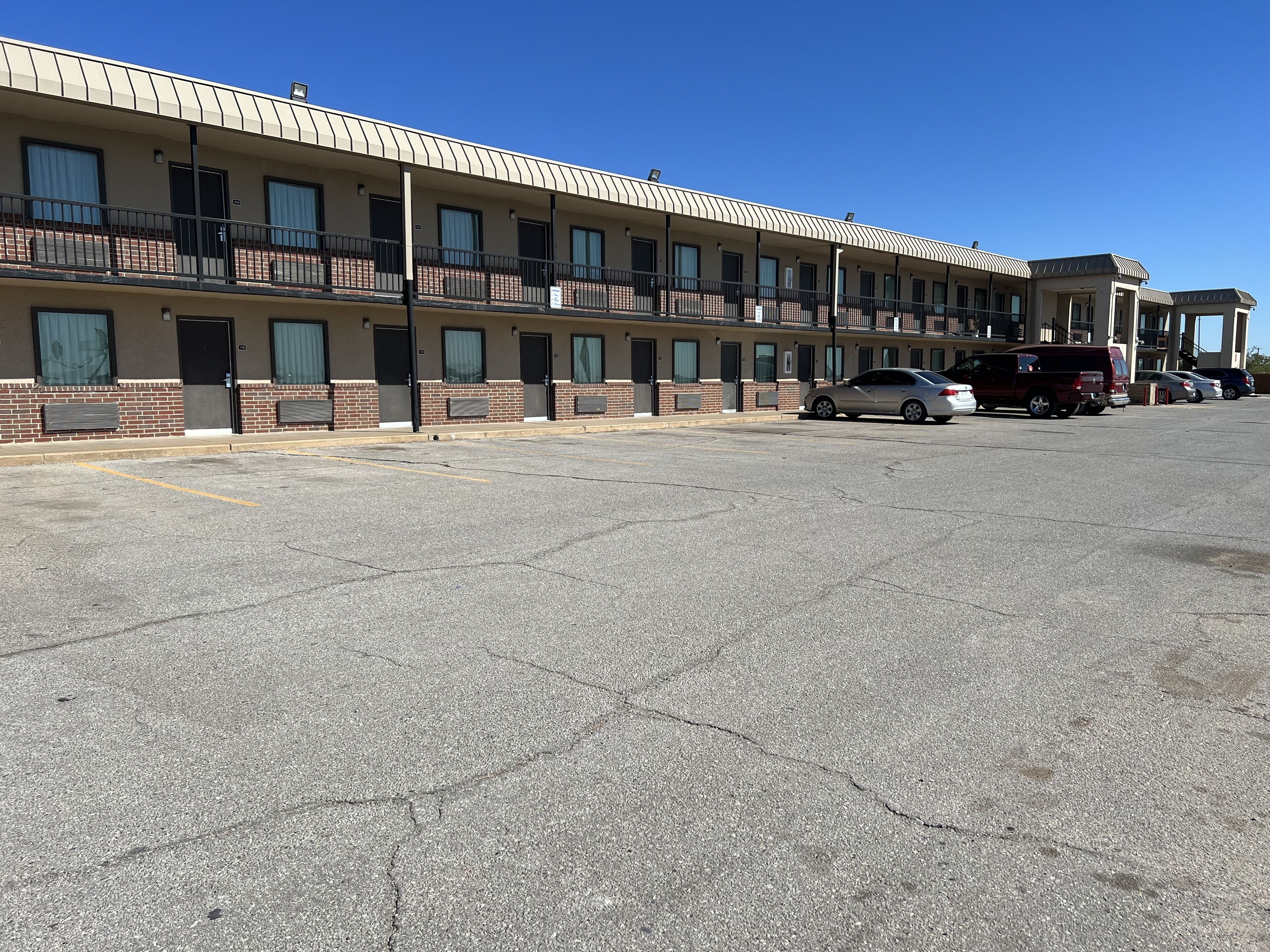 Un motel con una hilera de habitaciones, un estacionamiento y un cielo azul despejado.