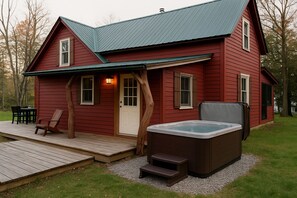 Une maison en bois rouge avec une terrasse, un jacuzzi et une petite table entourée de chaises.