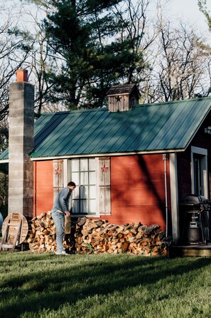 Une cabane rustique avec un toit en métal vert, une cheminée et une pile de bois de chauffage.