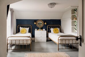 Une chambre avec deux lits simples, une commode blanche, un élément décoratif mural et une bibliothèque.
