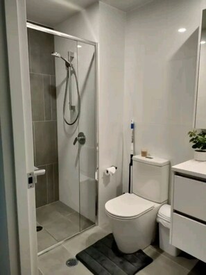 Un baño moderno con ducha de mampara de vidrio, inodoro y lavamanos.