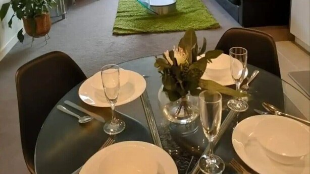 Una sala de estar moderna con un sofá, una mesa de comedor preparada para cuatro personas y un televisor.