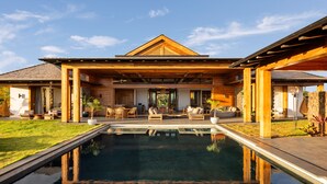 A modern house with a large pool, outdoor seating, and a covered patio area.