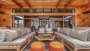 A spacious living area with wooden furniture, a central coffee table, and large windows.