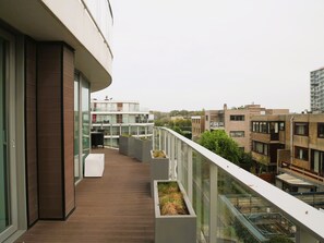 Un immeuble résidentiel moderne doté d’une terrasse en bois, de rampes de protection en verre et de plusieurs balcons.
