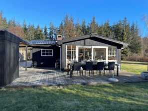 A wooden deck with outdoor furniture, a covered patio, and a view of a forested area.